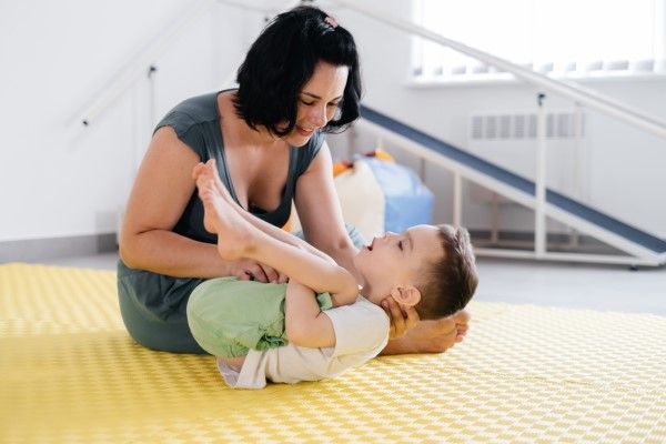 fisioterapeuta ayudando a un niño con terapia en la colchoneta de un gimnasio