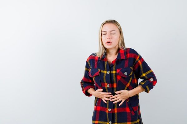 Mujer joven colocando sus manos sobre la barriga con cara de preocupación