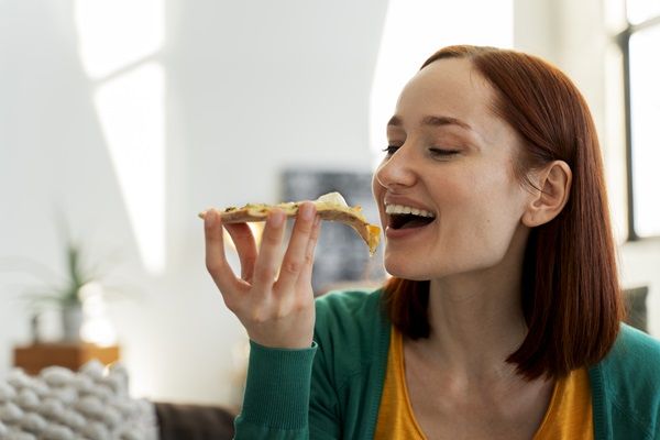 Aerofagia - Mujer joven de cabello castaño comiendo una rebanada de pizza