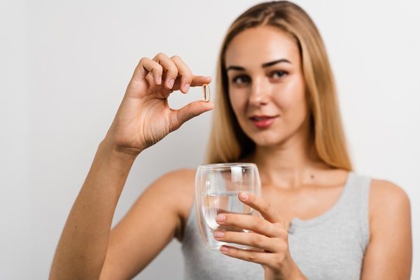 Mujer joven muestra un vaso de agua y una pastilla en su mano