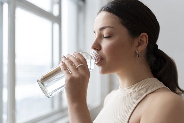 Mujer joven de cabello negro tomando agua en un envase de plástico