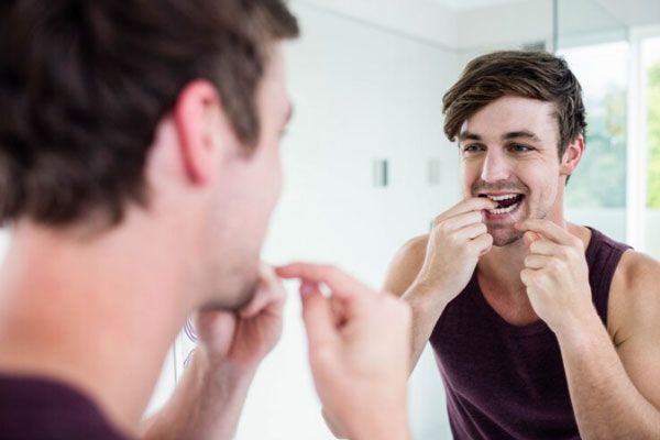 Hombre frente al espejo utiliza hilo dental para garantizar la limpieza de sus dientes y preservar la salud oral
