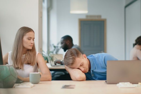 Hombre joven durmiendo sobre su brazo en el escritorio mientras está en el trabajo
