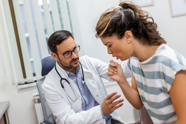 Mujer joven tosiendo en la consulta con un médico especialista