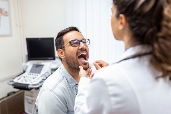 Doctora examina la boca y la garganta de un paciente con la ayuda de una espátula