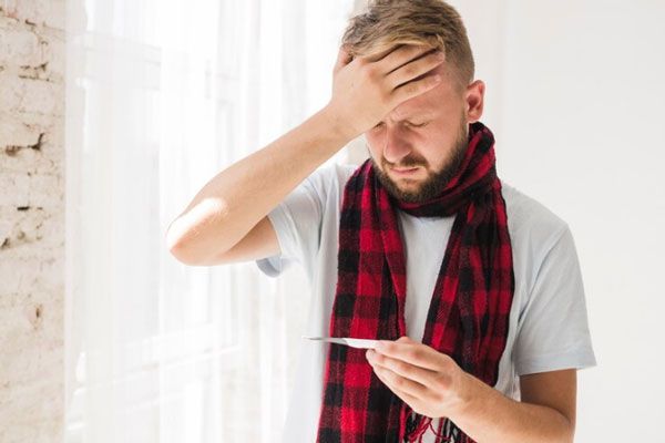 Hombre con fiebre y malestar general se toma la temperatura con un termómetro digital
