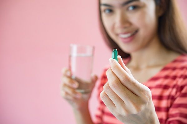 Mujer joven muestra un vaso de agua y una pastilla en su mano