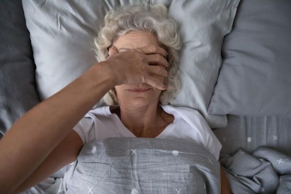 Parálisis del sueño - Mujer mayor somnolienta se cubre la cara tras despertar en la cama 