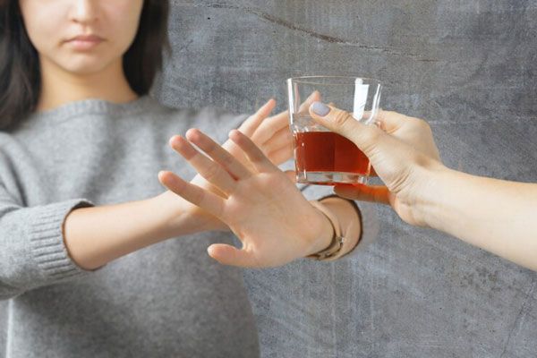 Joven mueve las manos en rechazo a un vaso de alcohol