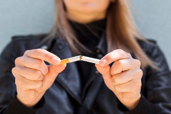 Vista frontal de una joven rompiendo un cigarrillo 