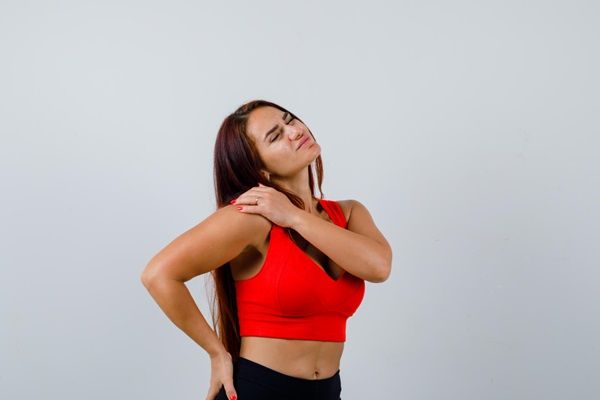 Descripción: Dermatomiositis – Mujer joven poniendo sus manos en el hombro y la cadera con gestos de dolor