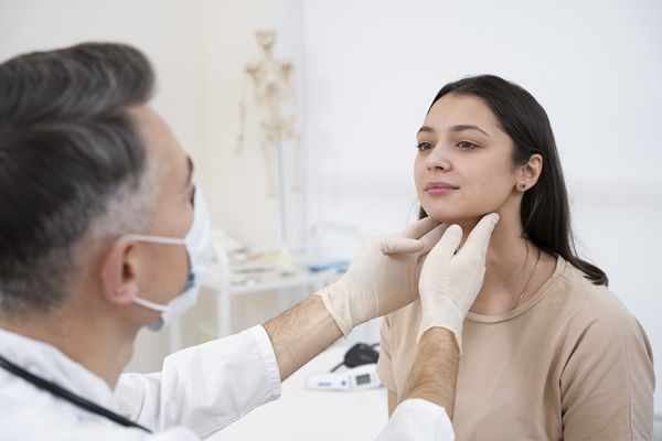 Enfermedad de Graves tratamiento natural - Médico especialista evaluando la zona de la glándula tiroides en una mujer joven
