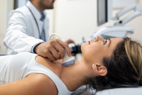 Enfermedad de Graves tratamiento natural - Médico utilizando un instrumento para evaluar la glándula tiroides en una paciente femenina