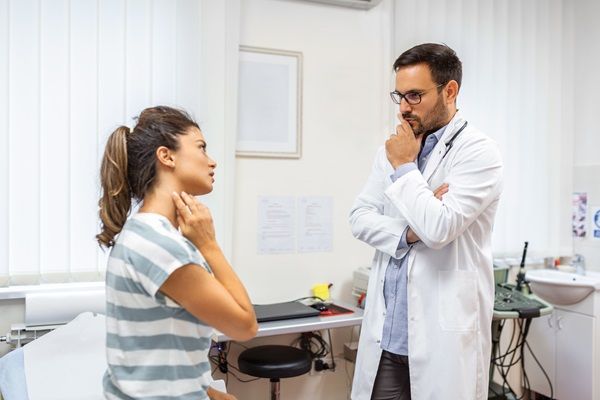 Mujer tocándose el cuello con gestos de dolor mientras conversa con el médico especialista que revisa su tiroides