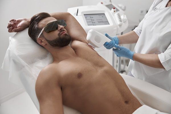 Esteticista realizando un tratamiento de depilación láser a un hombre joven