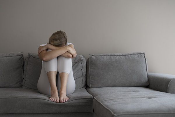 Síndrome de Cotard - Mujer sentada sobre el sofá reposando la cabeza en las piernas con actitud de tristeza