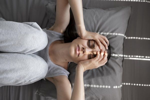 Mujer con cara de tristeza poniendo las manos en la cabeza mientras está acostada en la cama