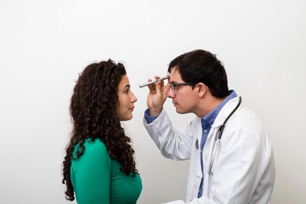 Médico utilizando una luz para evaluar los ojos de una mujer joven