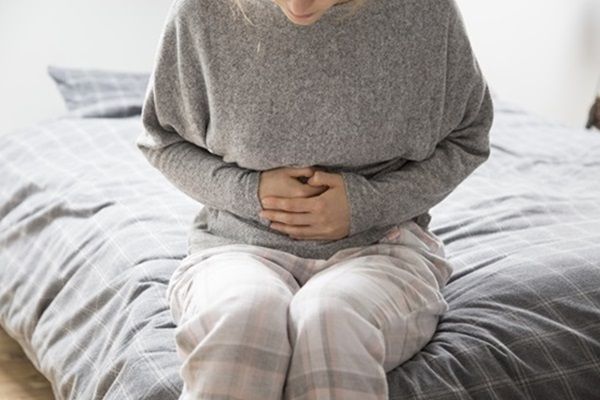 Vivir con la enfermedad de Addison - Mujer sentada en la cama tocándose con las manos el estómago
