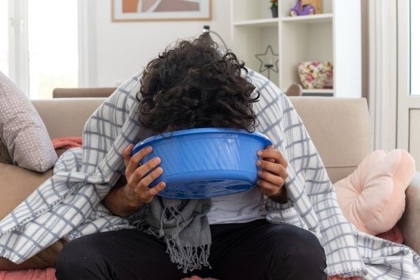Vivir con la enfermedad de Addison - Hombre sentado en el sofá sosteniendo una cubeta pegada a la cara para vomitar