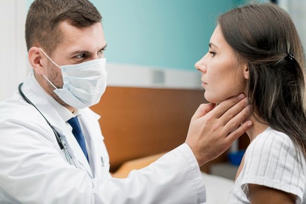 Enfermedad de Hashimoto dieta - Doctor evaluando la garganta y glándulas tiroideas de una mujer joven