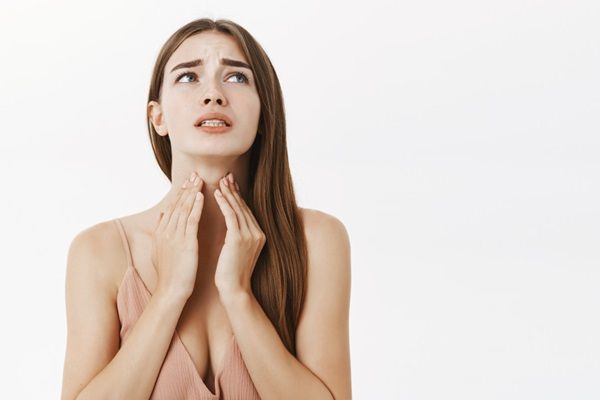 Enfermedad de Hashimoto dieta - Mujer tocándose la garganta con las manos mientras hace gestos de dolor