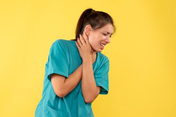 Mujer con bata de enfermera tocándose el cuello haciendo gestos de dolor