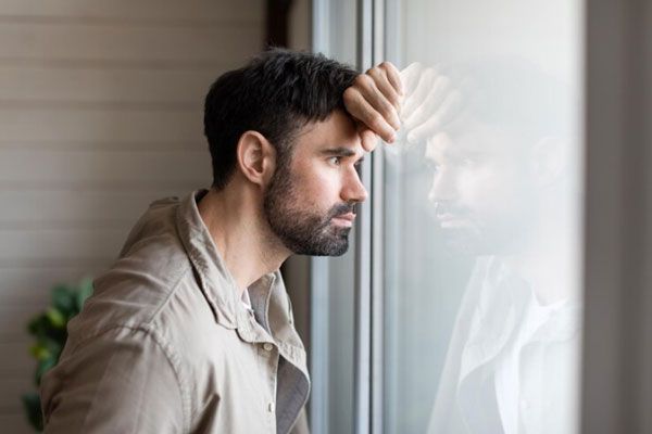 Esquizofrenia paranoide - Hombre desmotivado y con mirada inexpresiva se apoya sobre el vidrio de una ventana 