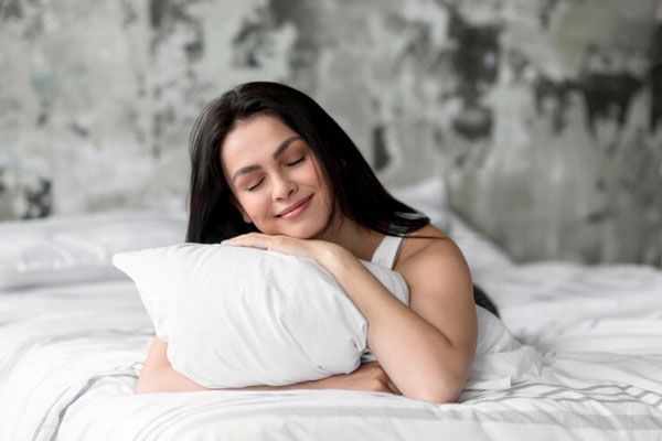 Mujer abraza una almohada mientras rescata la importancia del descanso y de dormir bien