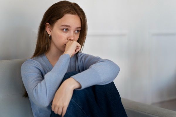 Mujer sentada en el sofá con cara pensativa y de tristeza