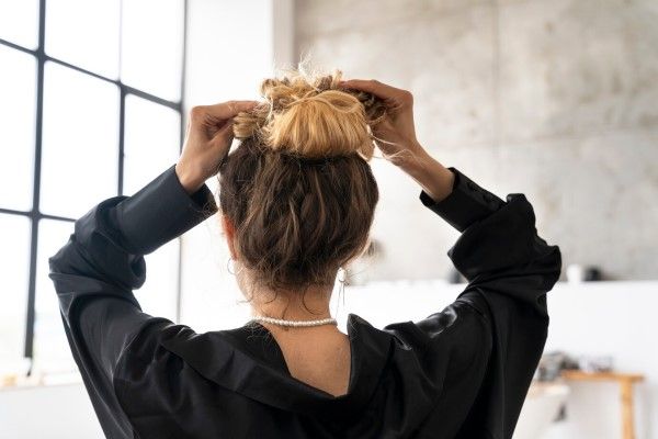 Mujer realizándose un peinado que causa tracción y puede provocar calvicie cicatricial en la línea frontal o las sienes