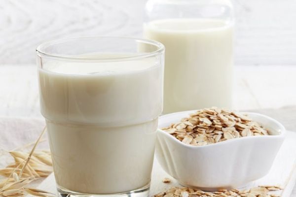 vasos de leche de avena al lado de unos granos de avena, un alimento para mantener sano nuestro corazón