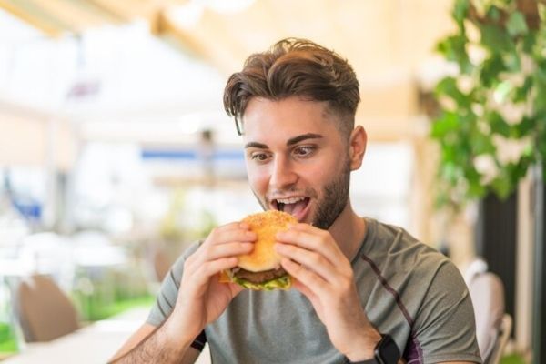 joven a punto de comerse una hamburguesa que contiene algún alimento ultraprocesado