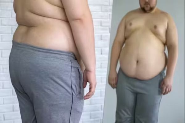 Tipos de obesidad - hombre obeso mirando los efectos de la obesidad en su cuerpo