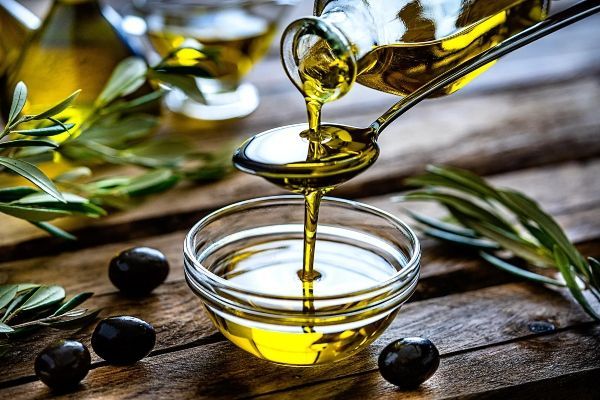 vertiendo aceite de oliva, alimento que ayuda a mantener nuestro corazón saludable, sobre una cuchara y a un recipiente