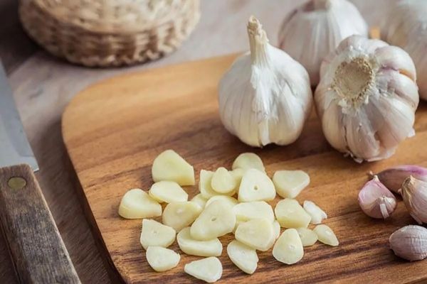 ajos enteros y picados sobre una mesa de madera, un alimento espectacular para controlar la grasa en el riego sanguineo