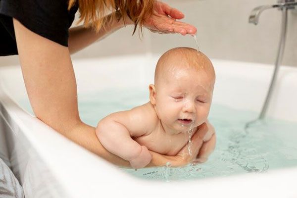 Cómo bajar la fiebre - Mujer bañando a un bebe en agua tibia para reducir la fiebre del infante