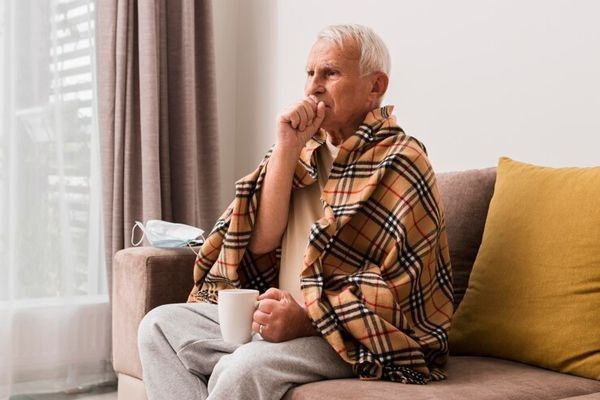 Bronquitis sin fiebre - hombre mayor sentado en el sofá tosiendo