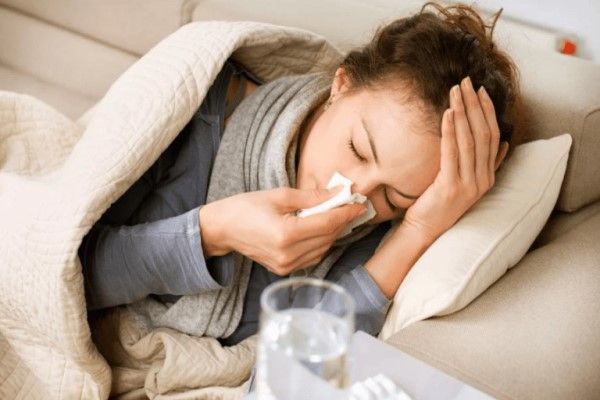 Bronquitis sin fiebre - mujer tumbada en el sofá envuelta en una manta sonándose la nariz