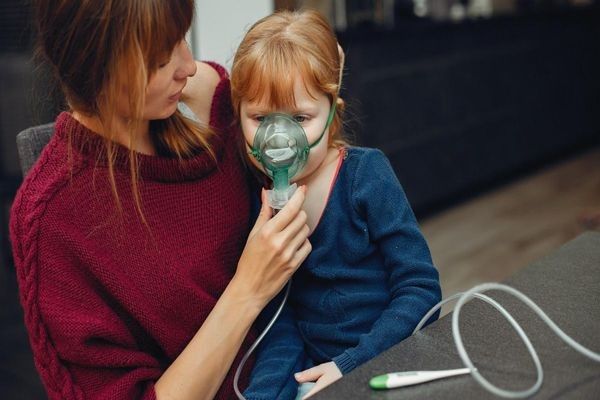 mujer ayudando a una niña a usar un nebulizador para mejorar su respiración por una enfermedad respiratoria
