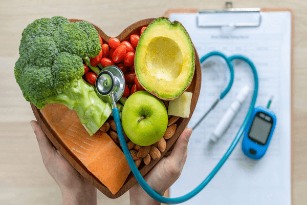 Colesterol bueno y malo - Persona con cesta de frutas y estetoscopio, resaltando la importancia de mantener el equilibrio entre el colesterol bueno y malo.