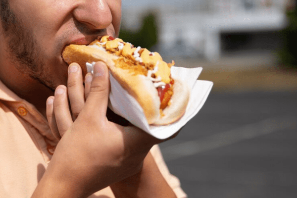 Hombre comiendo un hot dog, causa de trastornos digestivos por el consumo de comida chatarra