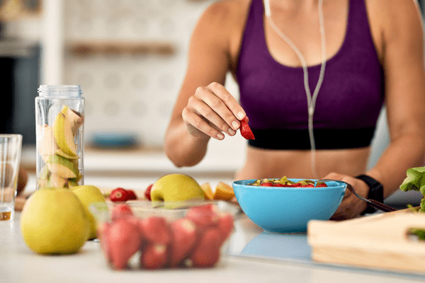 Dieta para bajar el colesterol - Mujer comiendo frutas frescas de un tazón, cumpliendo su dieta para bajar el colesterol