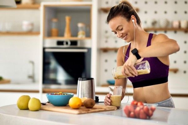 Dieta para ganar masa muscular - mujer sirviéndose en un vaso un batido proteínico