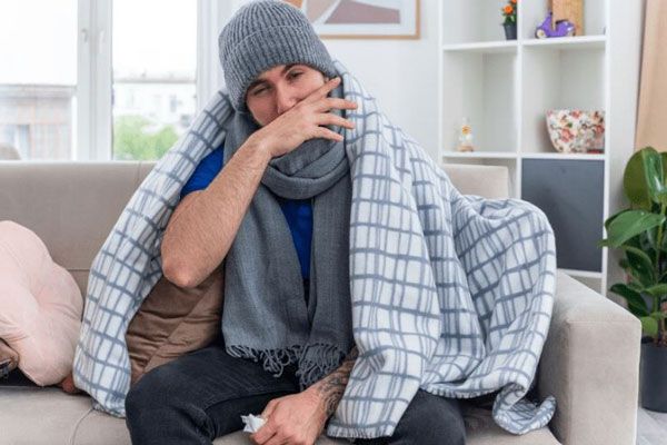 Hombre con alergia y escalofríos se abriga con una manta ligera para regular su temperatura corporal