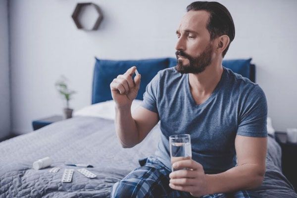 Cómo bajar la fiebre - Hombre con malestar general y fiebre se toma una pastilla de ibuprofeno o frenadol para aliviar los sintomas