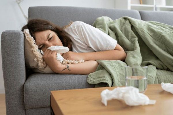 Cómo bajar la fiebre - Joven tumbada en un sofá con una manta con un pañuelo en la mano, sufriendo una enfermedad que le produce fiebre