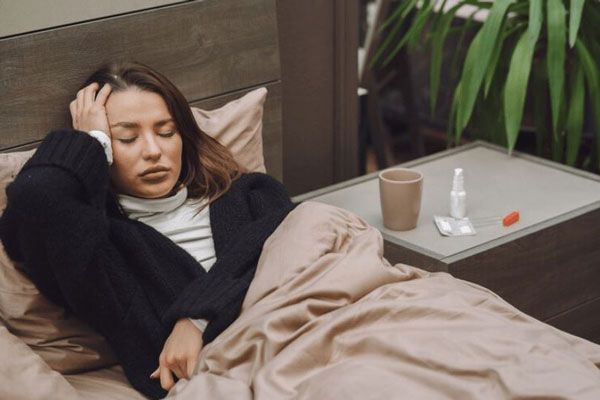 Mujer con temperatura elevada usando mucha ropa para irse a dormir algo que no hay que hacer cuando presentas un cuadro febril