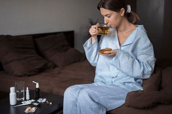 Cómo bajar la fiebre - Mujer bebiendo una infusión para mantenerse hidratada mientras tiene fiebre