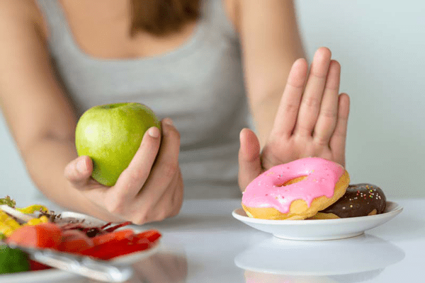 Mujer rechazando una dona para comer una manzana que ayuda a controlar el colesterol